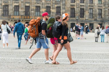 AMSTERDAM, NETHERLANDS - 8 Temmuz 2015: Sırt çantalı üç genç yürüyüşçü, şehrin meydanlarından birinde yürüyor.
