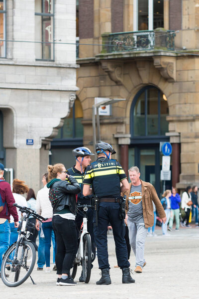 AMSTERDAM, NETHERLANDS - JULY 8, 2015: Two policemen bike, chatting with a young woman on a city street.