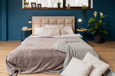 Koyu mavi duvarlı bir yatak odası. Lambalı ve saatli komodinlerin yanında.