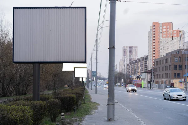 Caddedeki reklam panosunda direklerin arkasında arabalar ve evler var.
