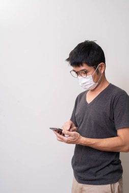Coronavirus gribini önlemek ve cep telefonu kullanmak için ameliyat maskesi takan Asyalı bir adam.