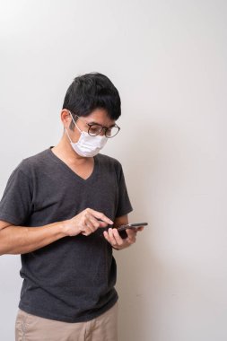 Coronavirus gribini önlemek ve cep telefonu kullanmak için ameliyat maskesi takan Asyalı bir adam.