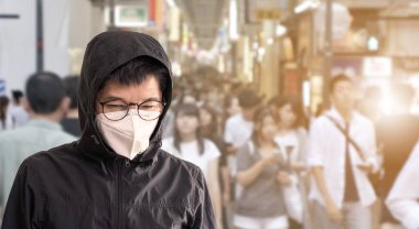 Grip hastalığını önlemek için cerrahi maske takan Asyalı bir adam Coronavirus ve seyahat eden insanların bulanık görüntüsü.