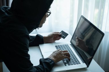 Siyah kapüşonlu ceketli, elinde kredi kartı olan ve labirent bilgisayarındaki şifreyi kontrol eden adamın arka tarafında. Hacker dolandırıcı konsepti