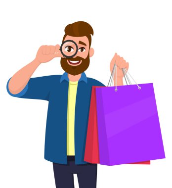 Alışveriş torbalarını gösteren mutlu genç adam. Elinde büyüteçle ya da büyüteçle bakan biri. Modern yaşam tarzı, dijital teknoloji, yeni satın alma, son trend konsepti.