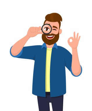 Genç adam büyüteçle bakıyor ve göz kırparken iyi bir hareket gösteriyor. Modayı takip eden kişi elinde büyüteç / lens tutuyor ve 