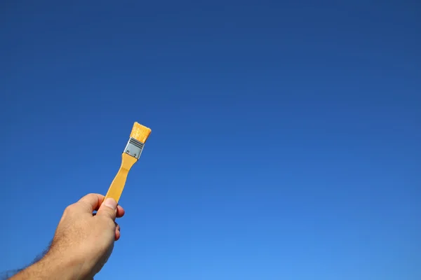 Man holding paint brash against of the blue sky — Stock Photo, Image