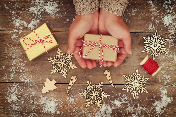 Manos de mujer sosteniendo regalos de Navidad en una mesa de madera —  Fotos de Stock