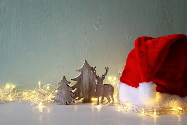 Nízké klíč dřevěné vánoční strom a jelen vedle santa klobouk — Stock fotografie