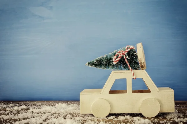 Ξύλινα αυτοκίνητο που μεταφέρουν ένα χριστουγεννιάτικο δέντρο σε χιονισμένο τραπέζι — Φωτογραφία Αρχείου