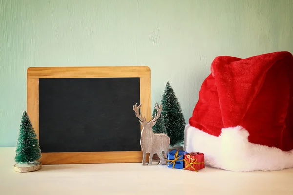 christmas trees and santa hat next to blank blackboard