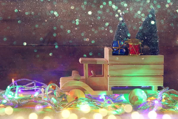 Fából készült autó szállító a karácsonyfa mellett garland fények — Stock Fotó