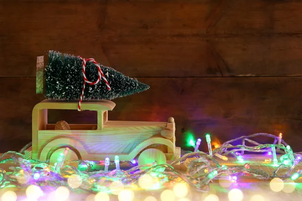 Coche de madera que lleva un árbol de Navidad sobre una mesa rústica — Foto de Stock