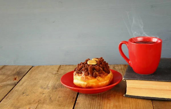 Пончик рядом с чашкой кофе и книгой — стоковое фото