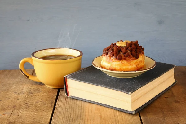 Пончик рядом с чашкой кофе и книгой — стоковое фото