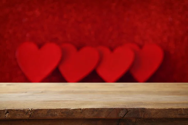 Empty wooden table in front of glitter red hearts background — Stock Photo, Image