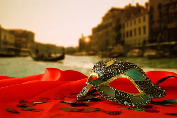 Masque vénitien sur tissu de soie rouge devant Venise floue — Photo