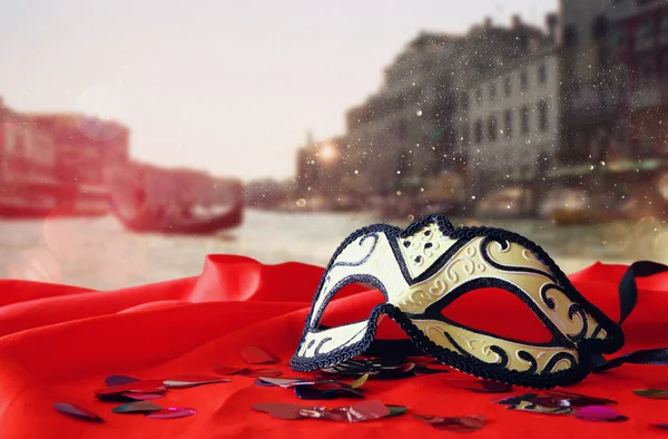 Venetian mask on red silk fabric in front of blurry Venice — Stock Photo, Image