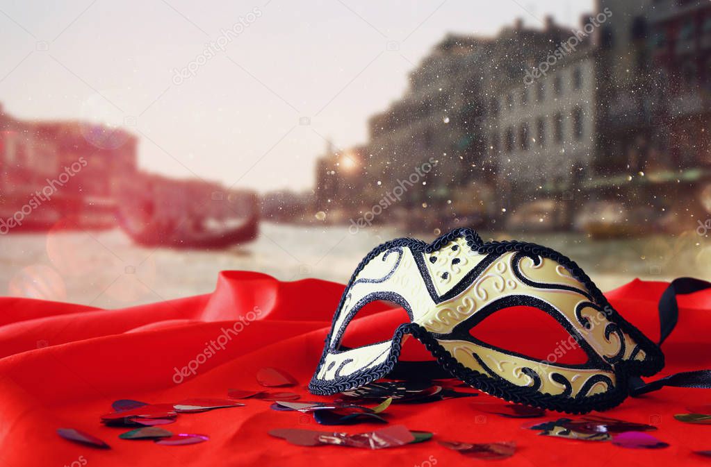 venetian mask on red silk fabric in front of blurry Venice