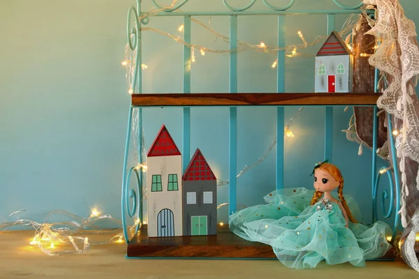 Boneca bonito e casas pequenas de madeira ao lado de luzes de guirlanda quentes — Fotografia de Stock