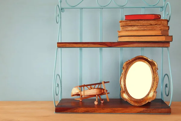 Vintage shelf with old wooden plane toy, books and blank photo frame