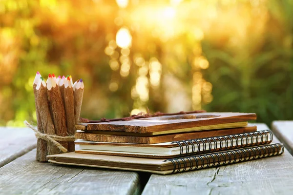 Afbeelding van notebooks, kleurrijke potloden op houten tafel buiten — Stockfoto