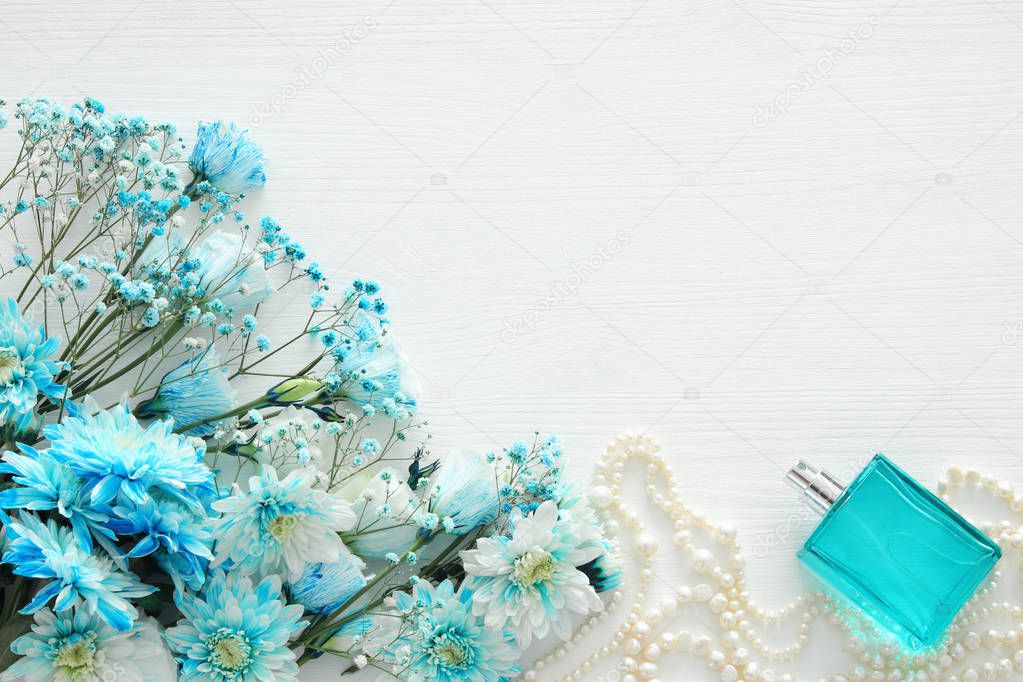 beautiful and delicate blue flowers arrangement next to pearls necklace and fresh perfume