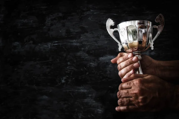 Χαμηλή βασική εικόνα ενός ανθρώπου που κρατώντας ένα Κύπελλο τρόπαιο πάνω από σκούρο φόντο — Φωτογραφία Αρχείου