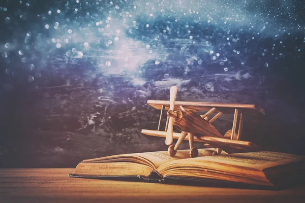 Toy plane and the open book on wooden table with glitter lights