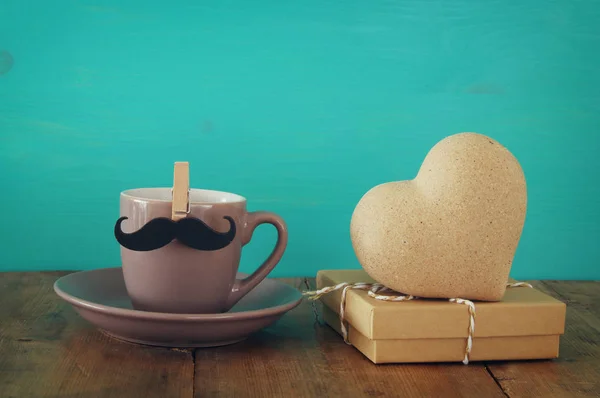 Cup of coffee with mustache next to wooden heart on the table — Stock Photo, Image