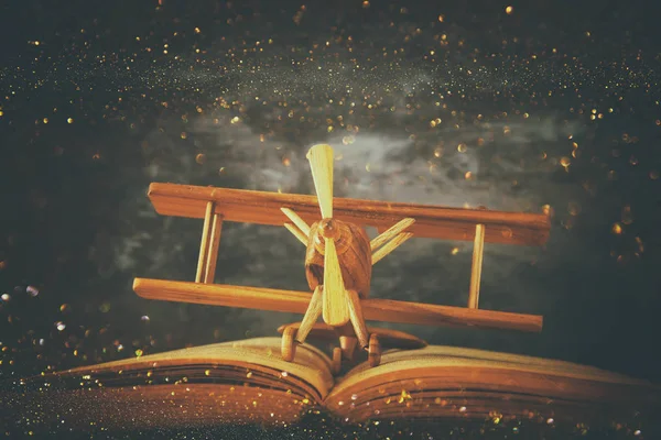Игрушечный самолет и открытая книга на деревянном столе с блестящими огнями — стоковое фото