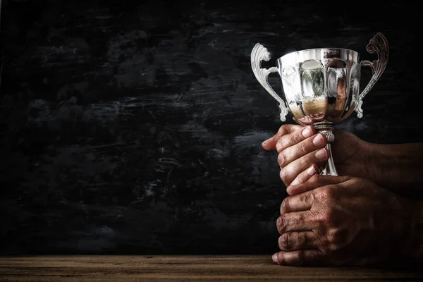 Låg nyckel bilden av en man som innehar en trophy cup över mörk bakgrund — Stockfoto