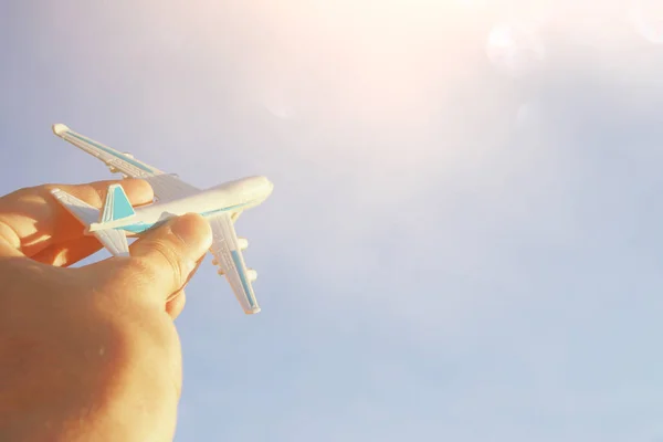 close up of man's hand holding toy airplane against blue sky