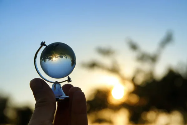 Mano maschile tenendo piccolo globo di cristallo davanti al tramonto — Foto Stock