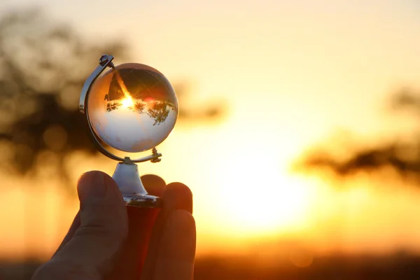 Main masculine tenant petit globe de cristal devant le coucher du soleil — Photo