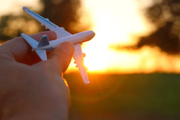 Close up af menneskets hånd holder legetøj fly mod solnedgang himmel - Stock-foto