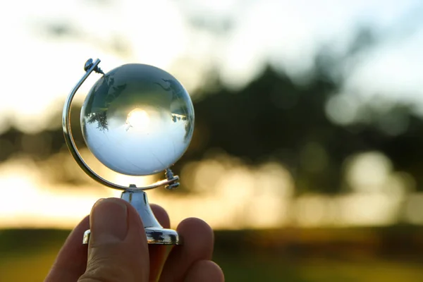 Mano masculina sosteniendo pequeño globo de cristal delante de la puesta del sol — Foto de Stock