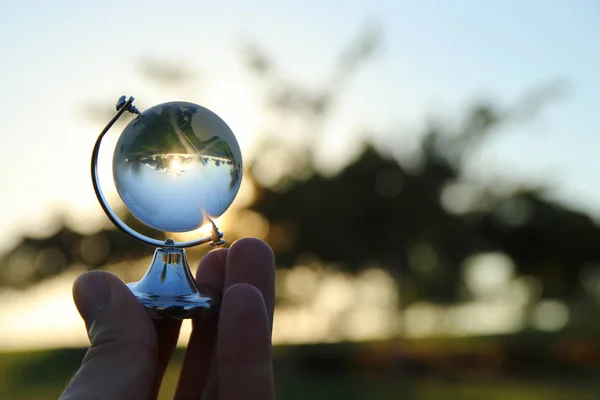 Manlig hand som håller små kristall världen framför sunset — Stockfoto