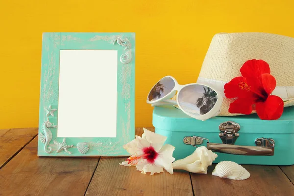 Sombrero Fedora, gafas de sol, flor de hibisco tropical junto a marco en blanco sobre mesa de madera — Foto de Stock