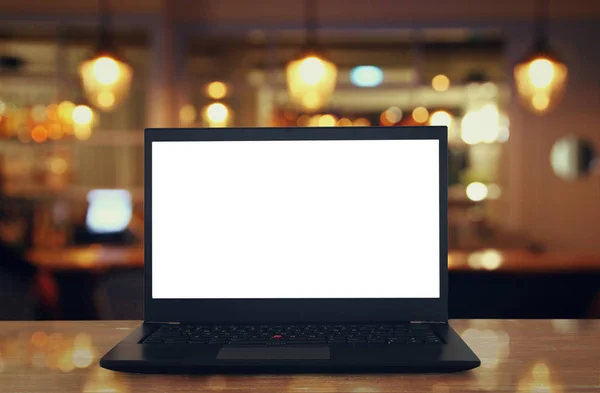Offener Laptop mit weißem Bildschirm auf Holztisch vor abstrakt verschwommenem Restaurantlicht Hintergrund. — Stockfoto