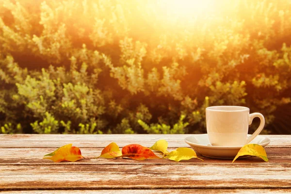 Tasse à café sur table en bois et feuilles d'automne devant le fond automnal — Photo