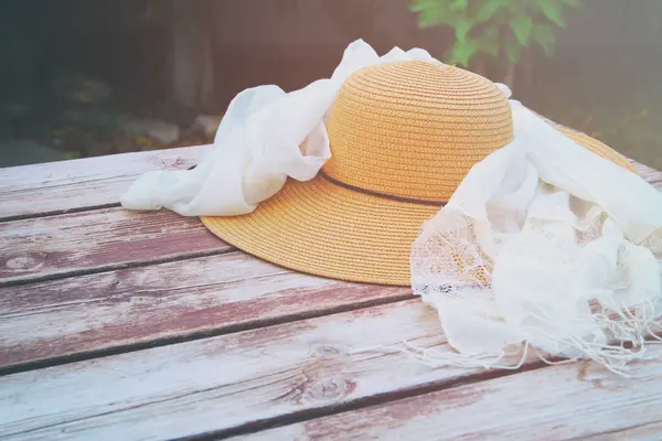 Летняя женская шляпа и нежный шарф на деревянном столе на открытом воздухе в парке — стоковое фото