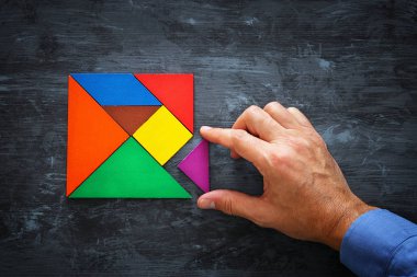 kayıp bir parça kare bir tangram tutan adamın el Bulmaca, ahşap masa üzerinde