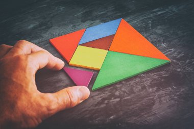 kayıp bir parça kare bir tangram tutan adamın el Bulmaca, ahşap masa üzerinde
