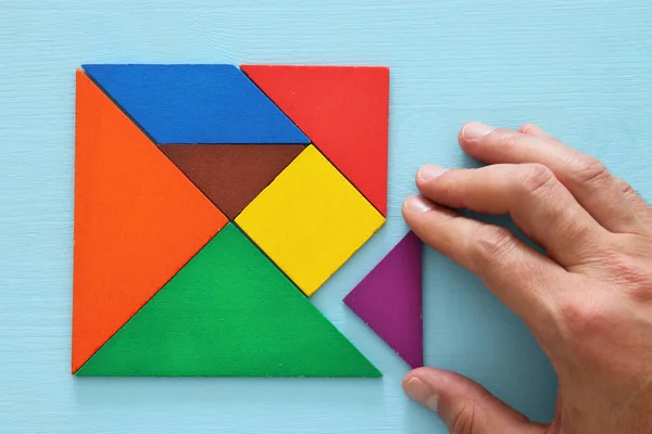 Ruka držící chybějící kousek v čtvercové tangram puzzle dřevěný stůl — Stock fotografie