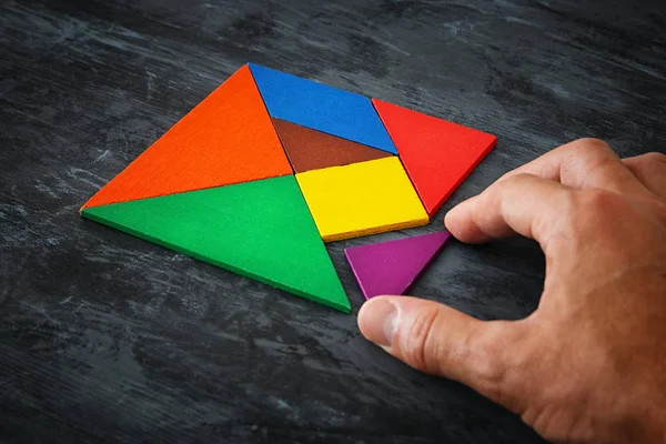 Iemands hand met een ontbrekende stuk in een vierkante tangram puzzel, over houten tafel — Stockfoto