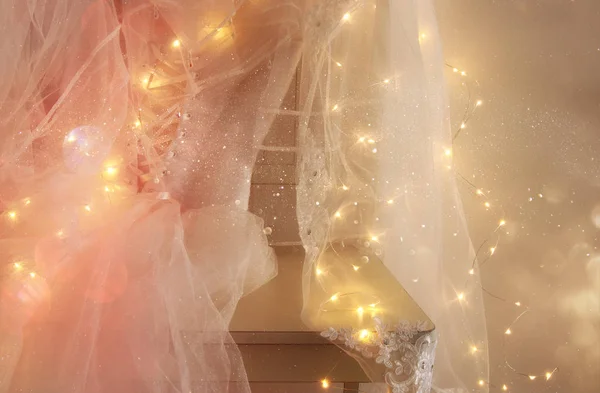 Vestido de noiva branco bonito e véu na cadeira com luzes de guirlanda de ouro — Fotografia de Stock