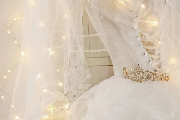 Vestido de noiva branco bonito e véu na cadeira com luzes de guirlanda de ouro — Fotografia de Stock