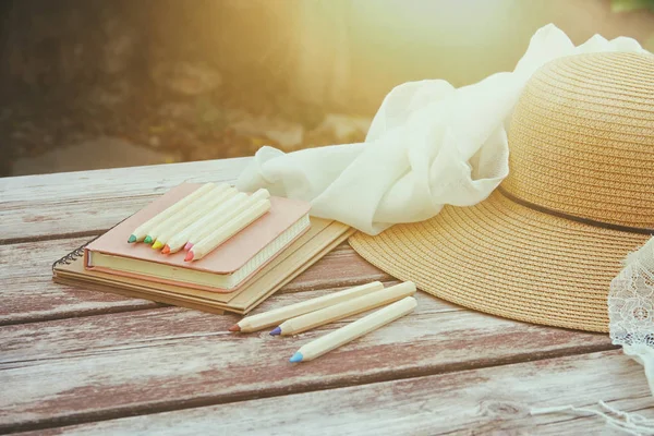 Books, colorful pencils and female hat on old wooden table outdoor in the park — Stock Photo, Image