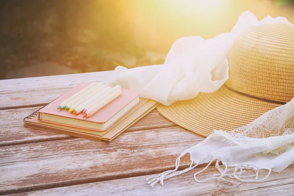 Books, colorful pencils and female hat on old wooden table outdoor in the park — Stock Photo, Image